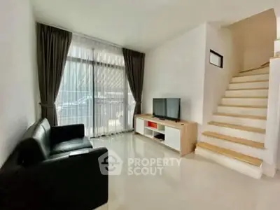 Modern living room with sleek black sofa, TV unit, and staircase, featuring large window with curtains.