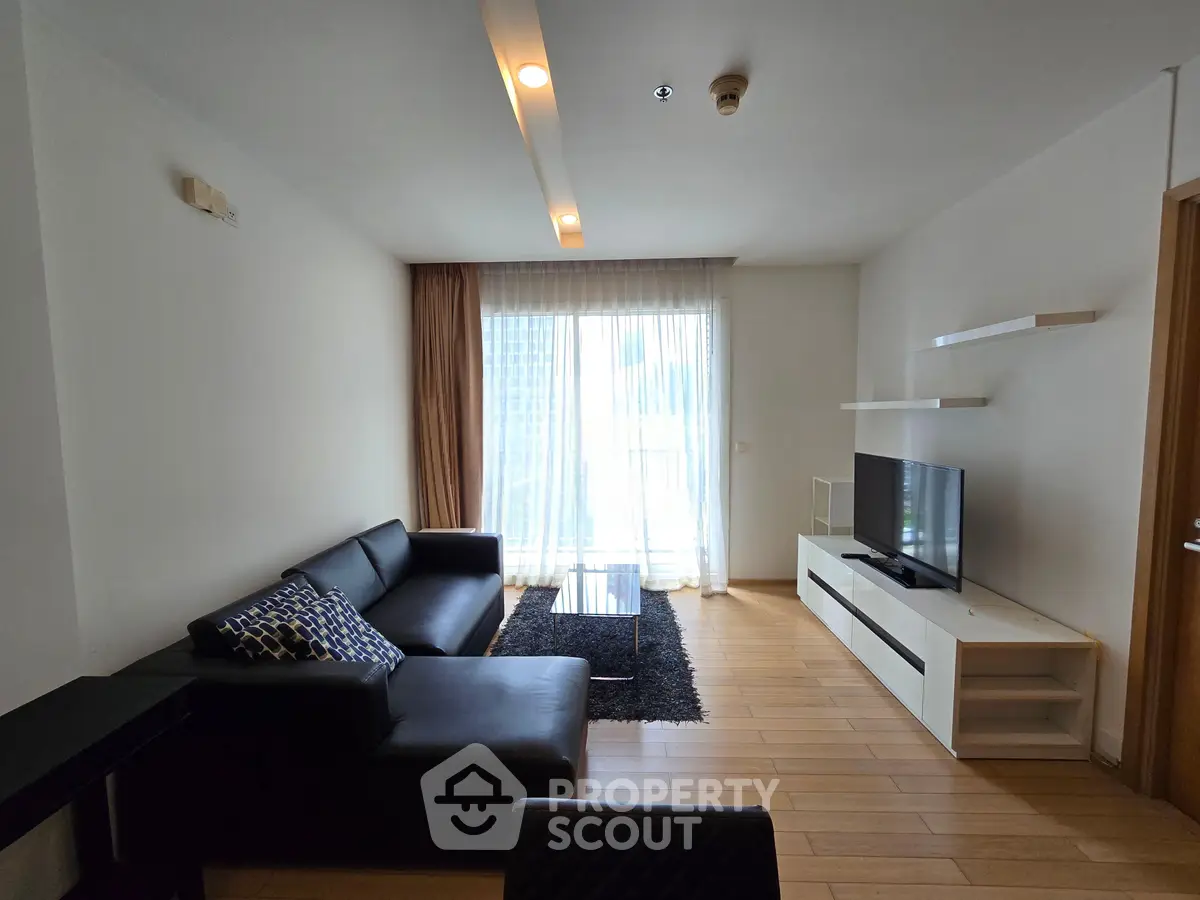 Modern living room with sleek black sofa, TV, and natural light from large window.