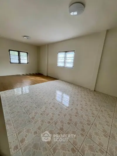 Spacious room with tiled and wooden flooring, ample natural light from multiple windows.