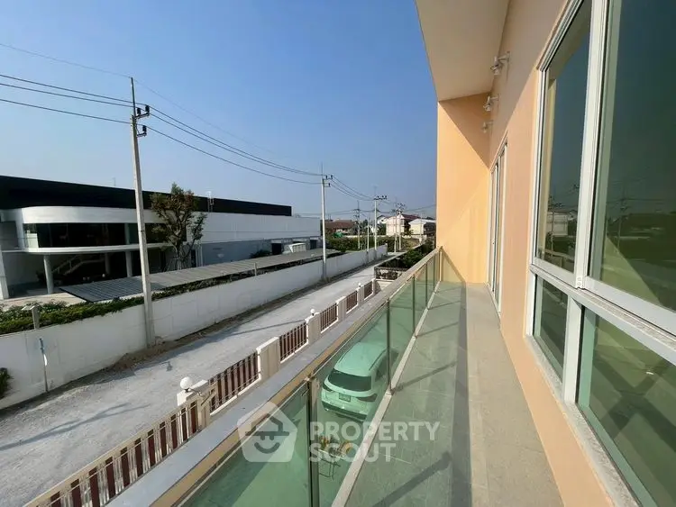 Spacious balcony with glass railing offering a serene street view in a modern residential area.