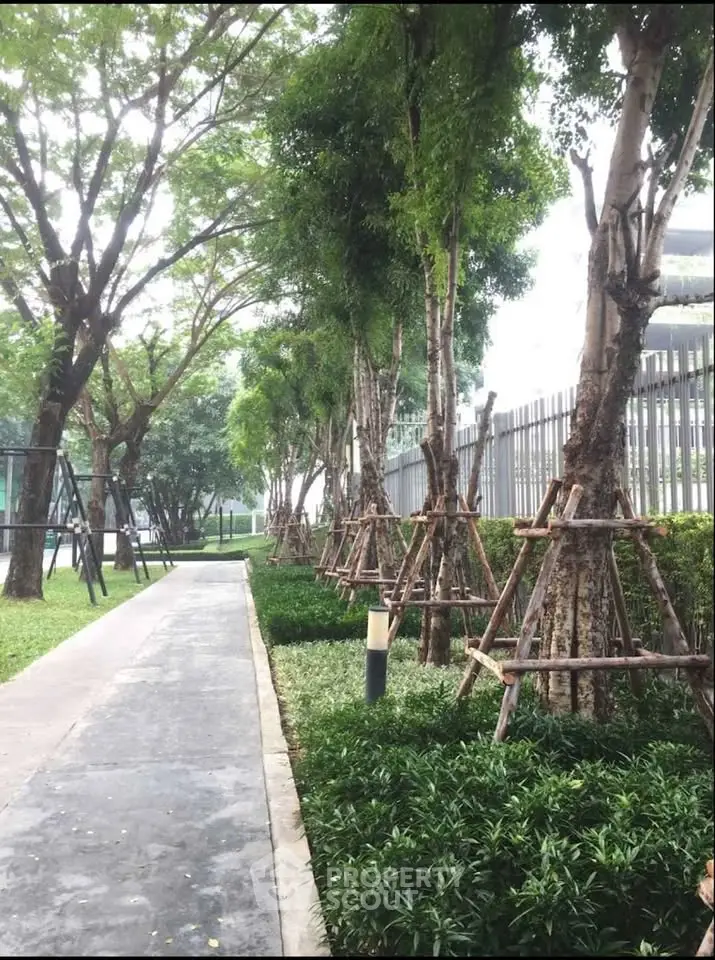 Lush garden pathway with mature trees and manicured greenery in modern residential complex.