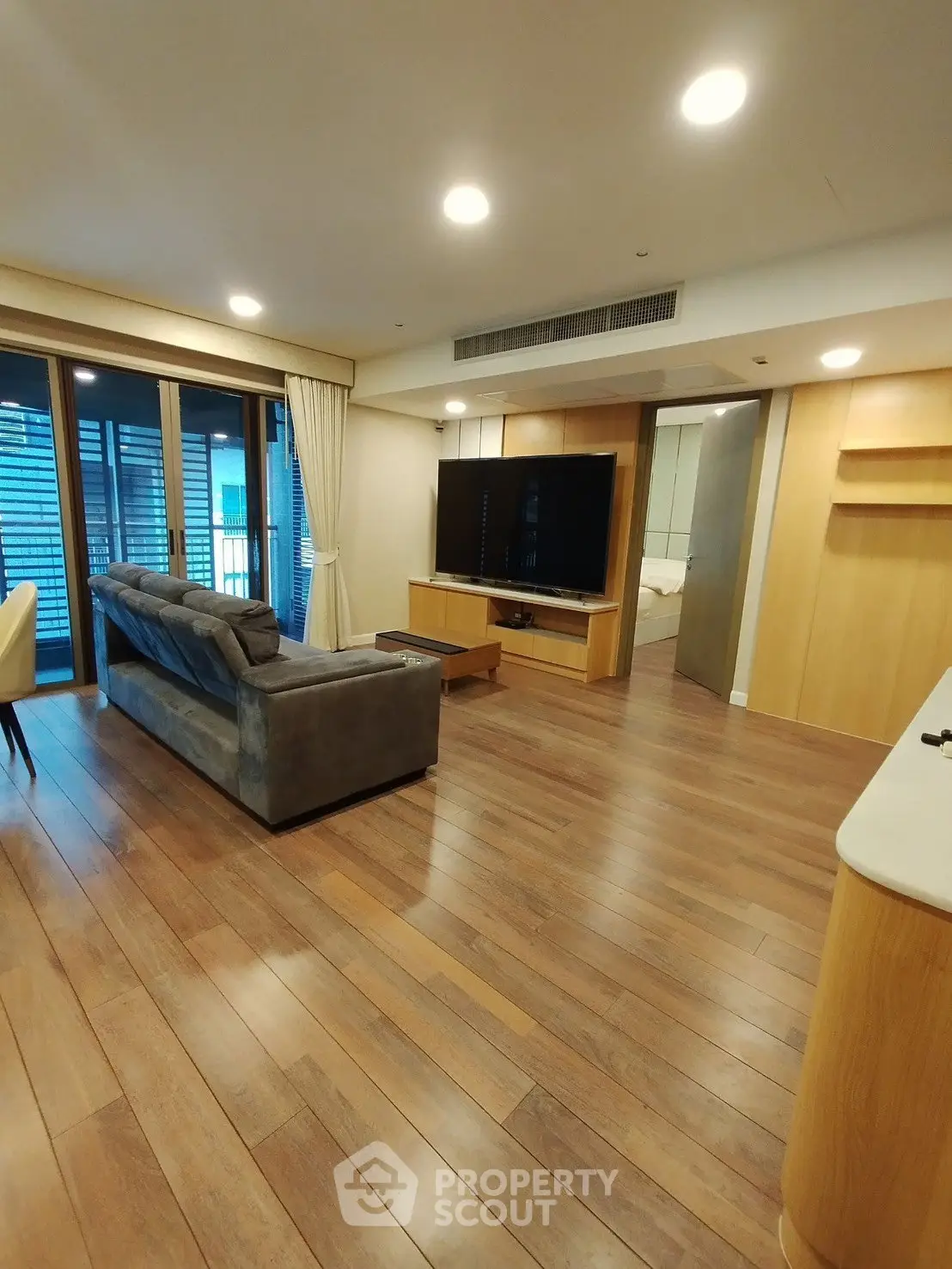 Spacious living room with modern decor and large TV, featuring wooden flooring and ample natural light.