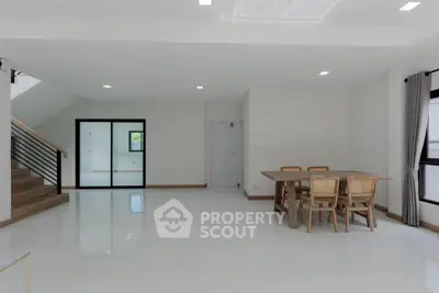 Spacious modern living room with dining area and staircase, featuring minimalist design and natural light.
