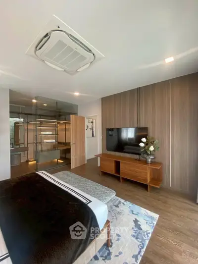 Modern bedroom with stylish decor and glass-enclosed bathroom, featuring wooden flooring and sleek furniture.