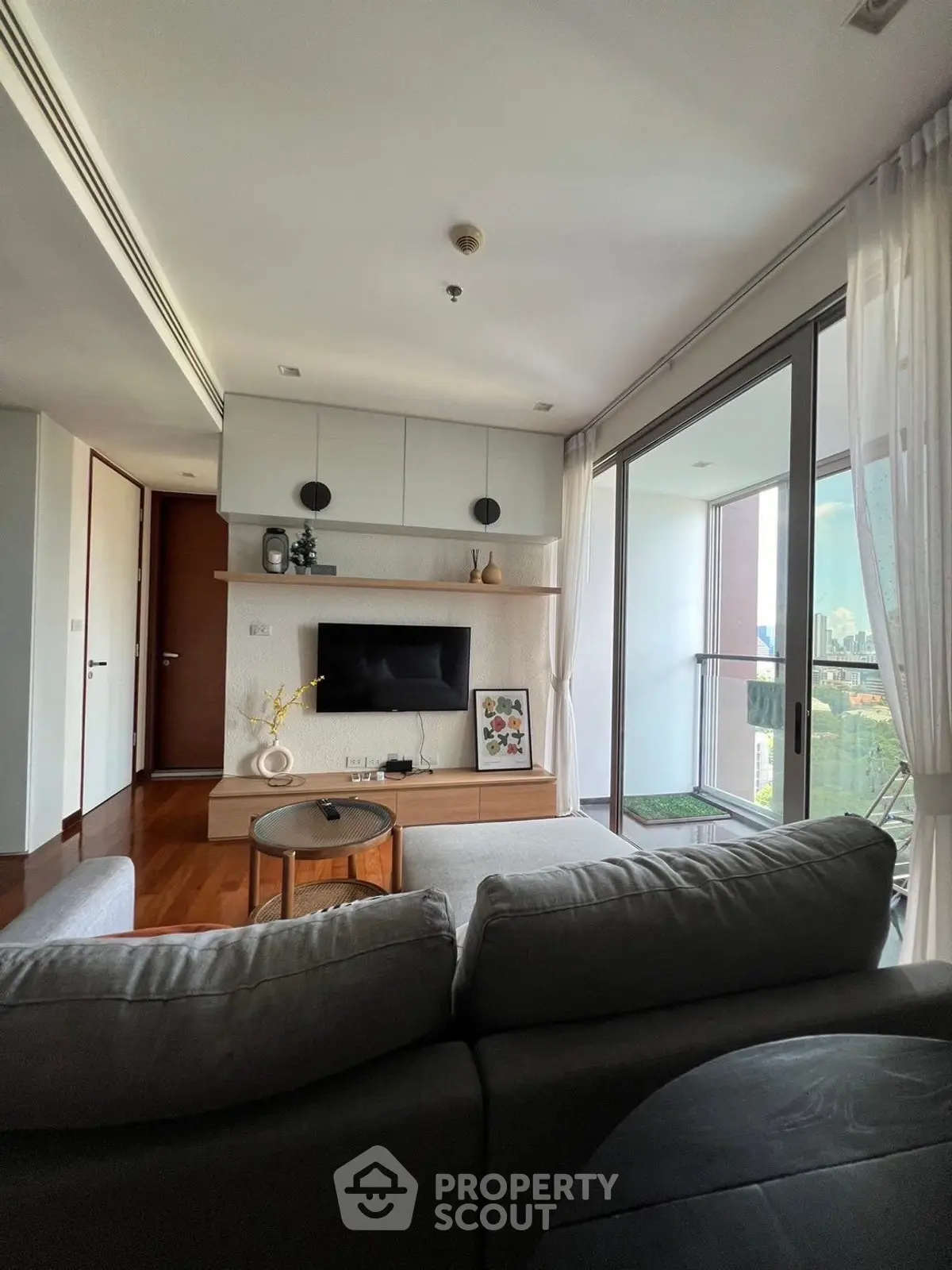 Modern living room with balcony view, stylish decor, and natural light in a high-rise apartment.