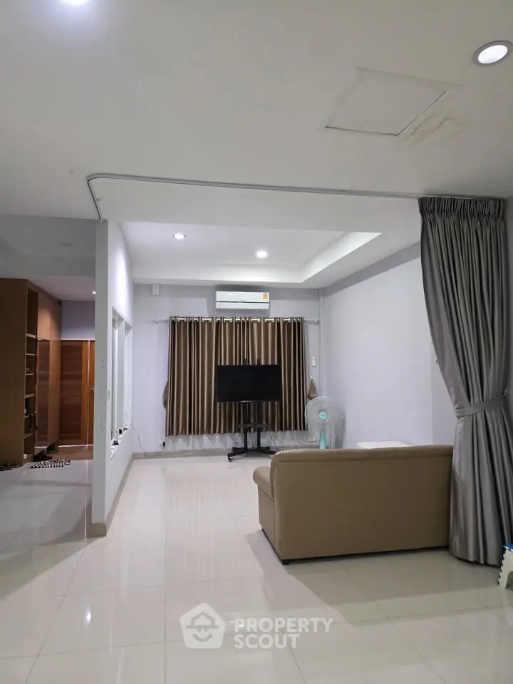 Spacious living room with modern decor and sleek flooring, featuring a comfortable sofa and large TV setup.