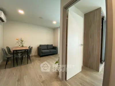 Modern apartment interior with cozy living room and dining area, featuring sleek furniture and wooden flooring.