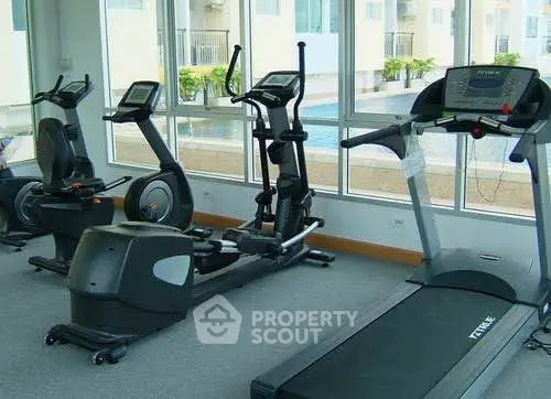 Modern gym with cardio equipment and pool view in luxury apartment complex.