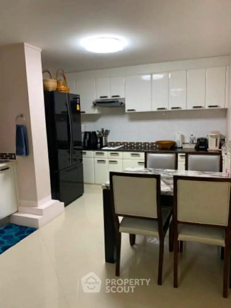 Modern kitchen with sleek white cabinets and dining area, featuring a black refrigerator and stylish decor.