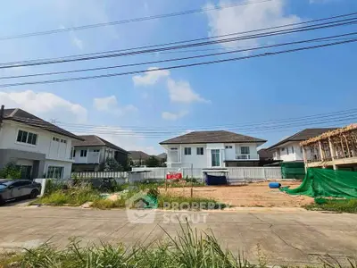 Spacious residential plot with modern houses and clear blue sky, ideal for new home construction.
