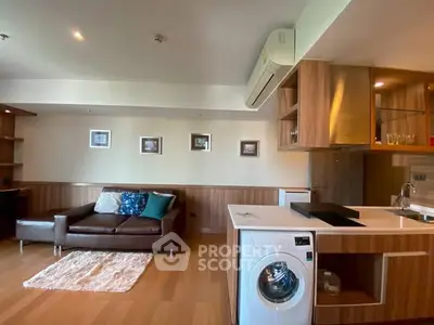 Modern living room with stylish kitchen and washing machine, featuring wooden flooring and cozy sofa.