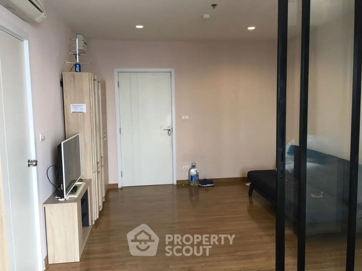 Modern living room with wooden flooring and glass partition, featuring a sleek TV setup.