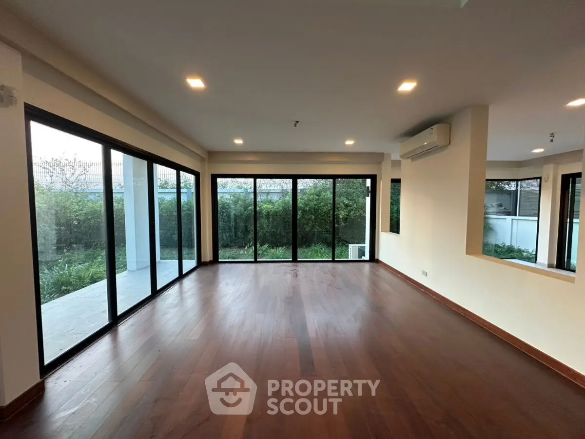 Spacious living room with hardwood floors and large windows overlooking a lush garden.
