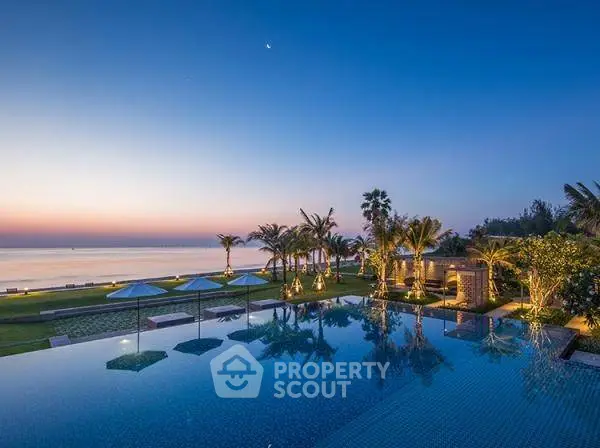 Luxurious beachfront property with stunning infinity pool and ocean view at sunset.