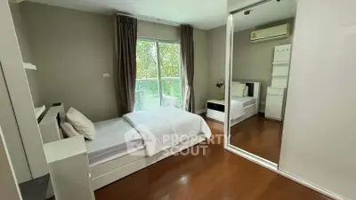 Spacious bedroom with mirrored closet and large window overlooking greenery.