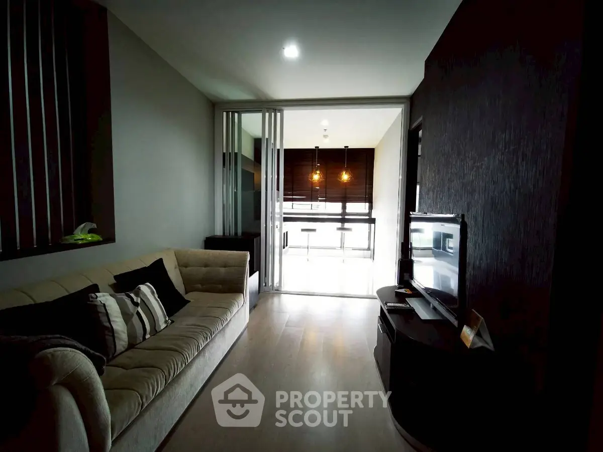 Modern living room with cozy sofa and sleek TV setup, leading to a bright balcony area.