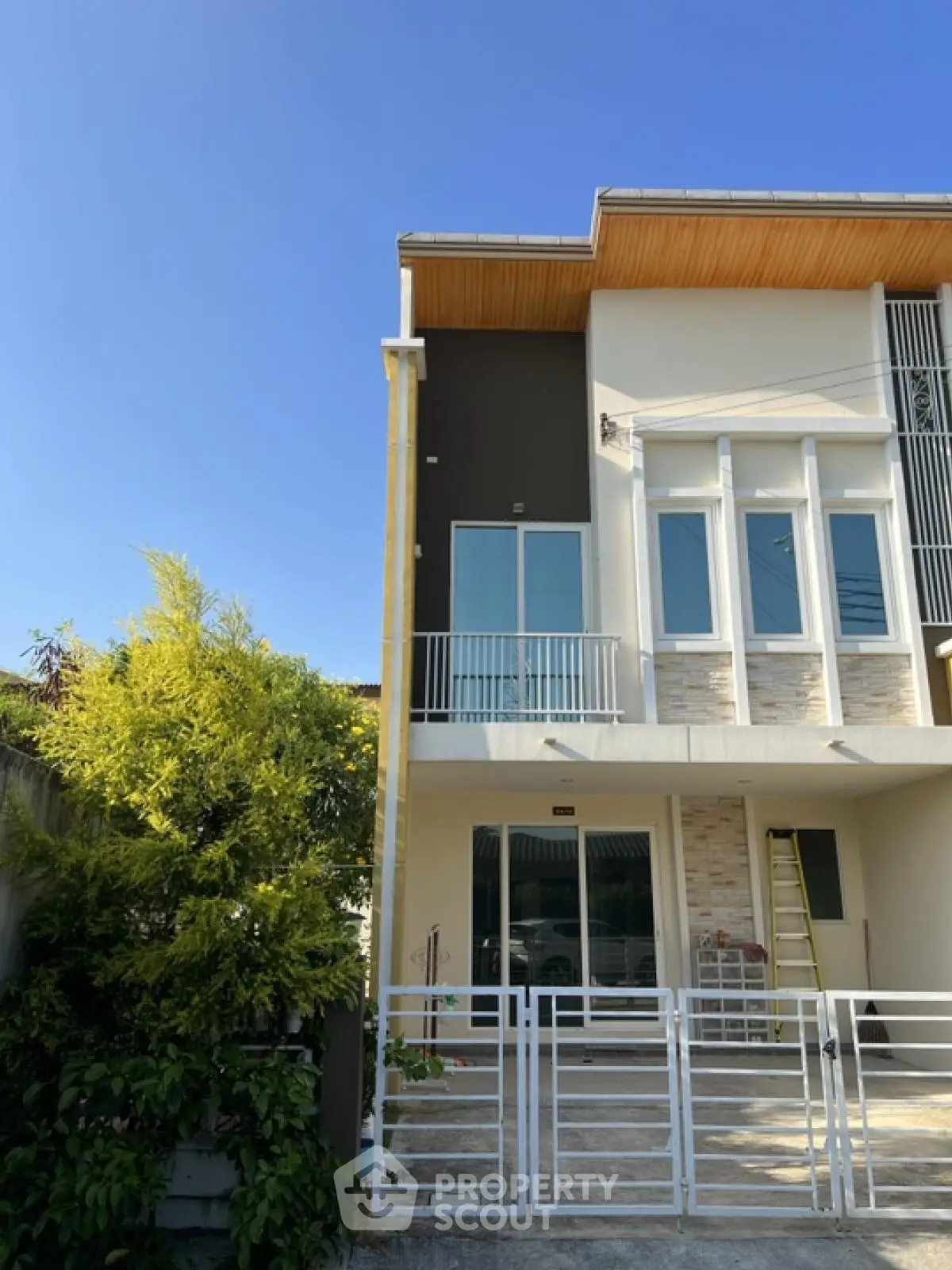 Modern townhouse exterior with balcony and gated entrance under clear blue sky.