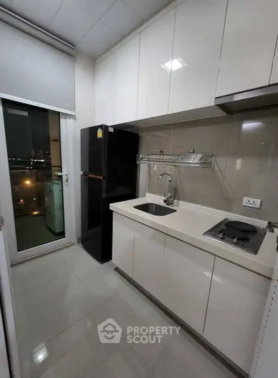 Modern kitchen with sleek cabinetry and compact design, featuring a black fridge and electric stove.