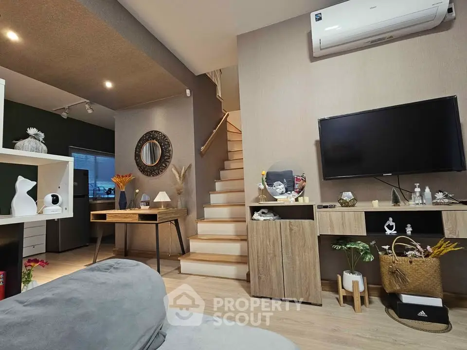 Modern living room with stylish decor and staircase, featuring air conditioning and wooden furniture.