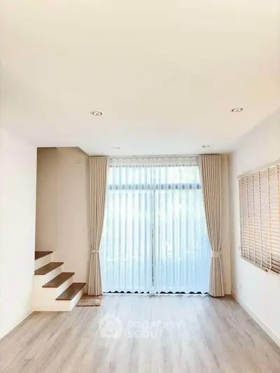 Bright and airy living room with floor-to-ceiling windows and elegant curtains, featuring a modern staircase.