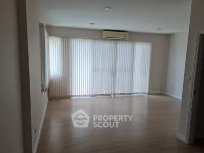 Spacious empty living room with wooden flooring and large windows.