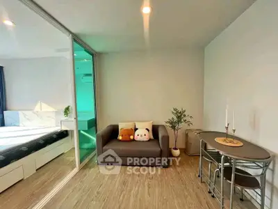 Modern living room with cozy sofa and dining table, adjacent to a stylish bedroom with glass partition.
