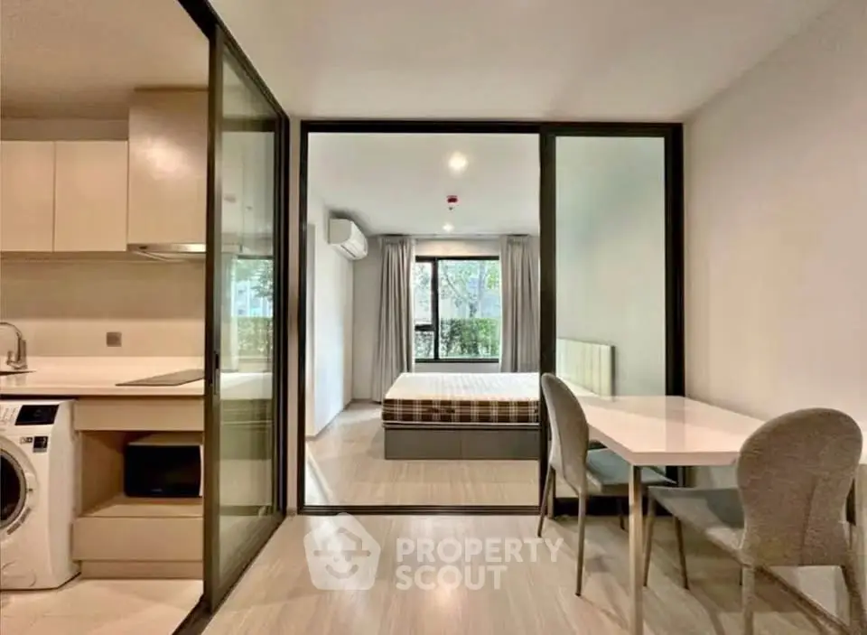 Modern studio apartment with glass partition, featuring compact kitchen and cozy bedroom.