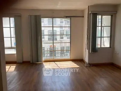 Spacious sunlit room with large windows and wooden flooring in modern apartment.