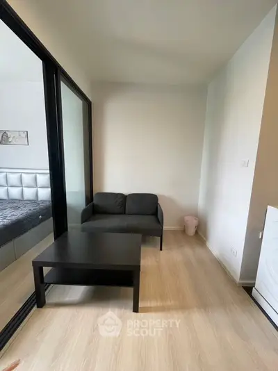 Cozy small living area with modern black sofa and table, adjacent to a bedroom with mirrored sliding doors.