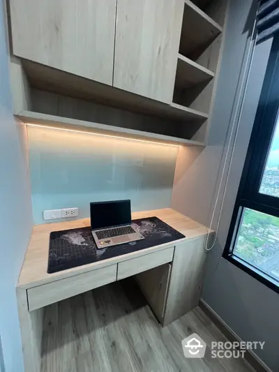 Modern study nook with built-in desk and shelves, featuring a sleek laptop setup and window view.