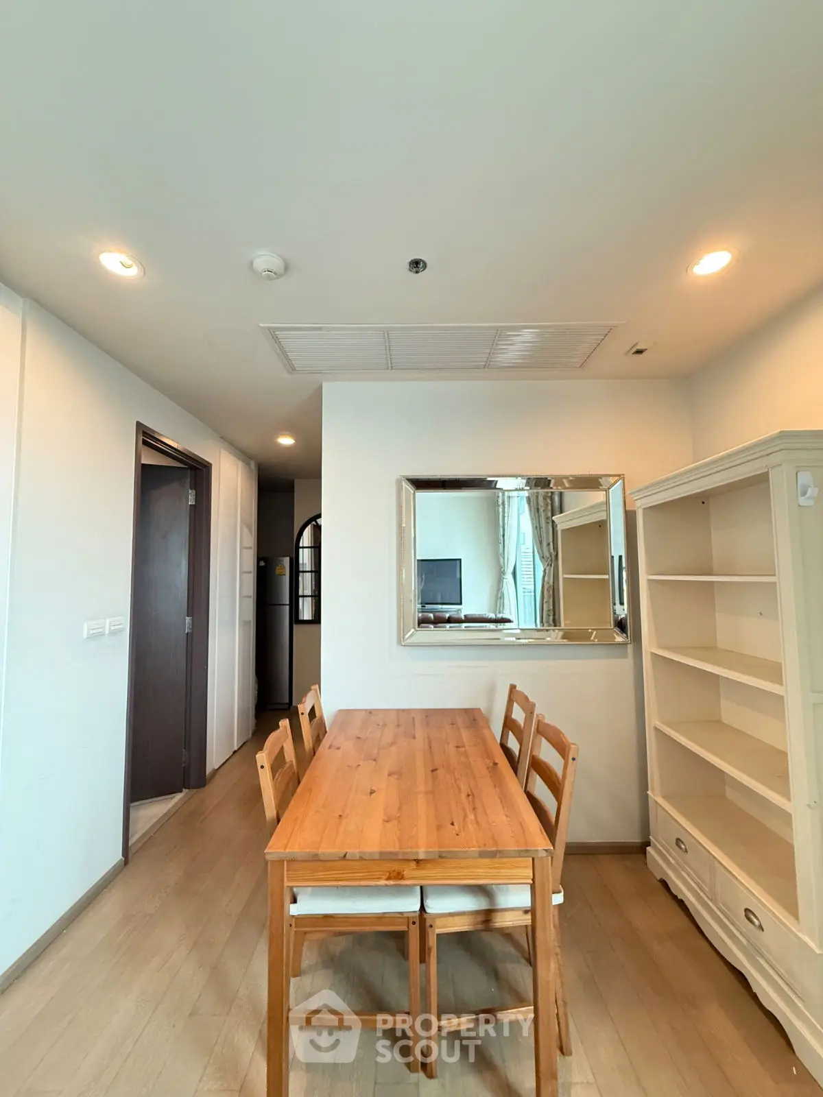 Modern dining area with wooden table and chairs, bright lighting, and elegant mirror.