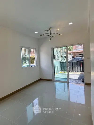 Bright empty room with modern chandelier and large windows overlooking a street view.