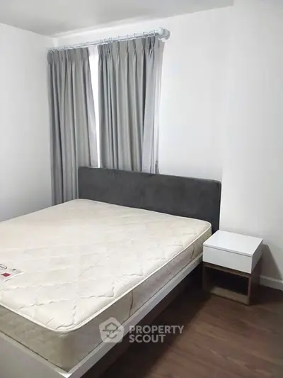 Cozy bedroom with modern bed and nightstand, featuring elegant curtains and wooden flooring.