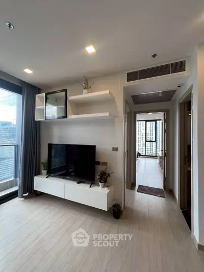 Modern living room with sleek TV unit and large windows offering city views.
