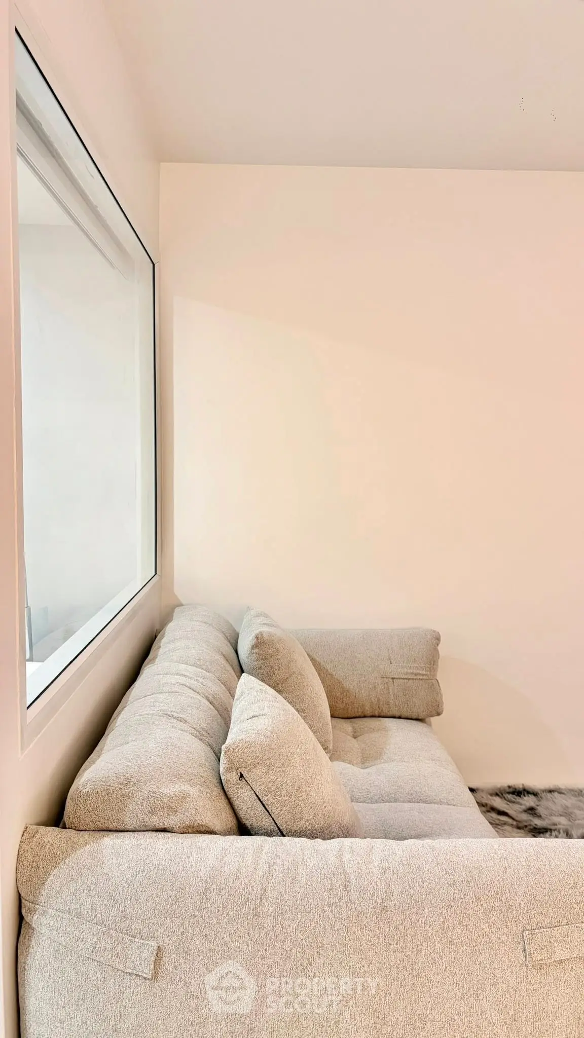 Cozy living room with plush beige sofa and large window, perfect for relaxation.
