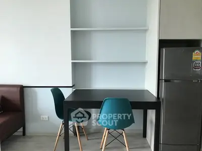 Modern dining area with teal chairs and sleek refrigerator in a compact apartment.