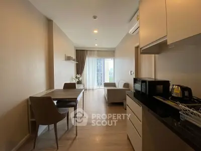 Modern open-plan living room with dining area and kitchenette, featuring sleek furniture and natural light.