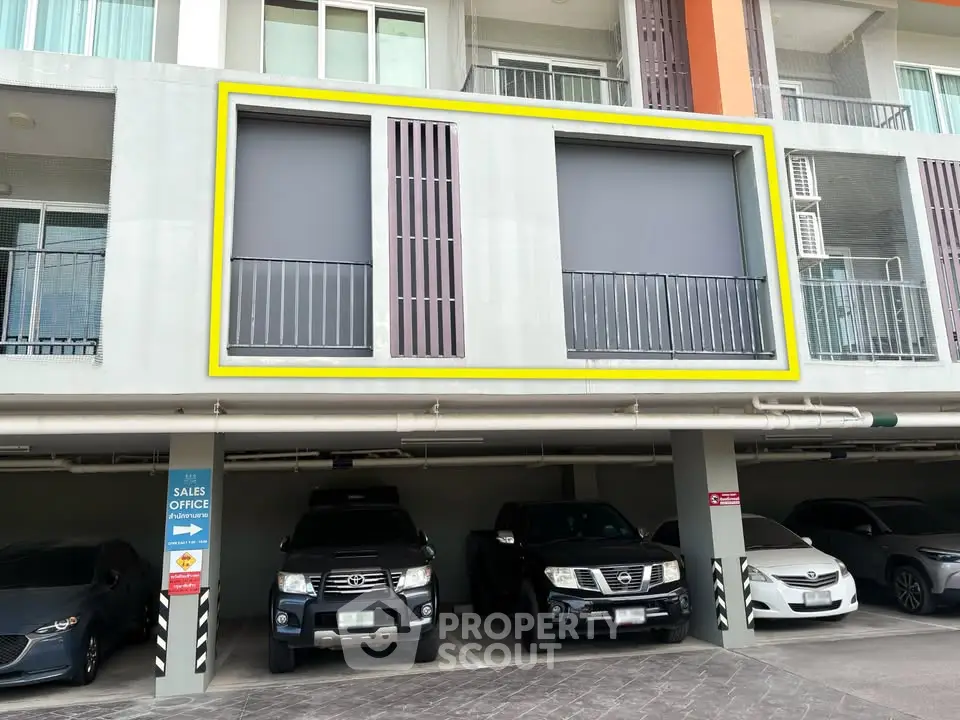 Modern apartment building with parking area and sales office sign, showcasing urban living convenience.