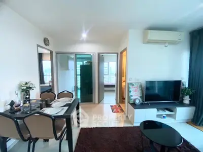 Modern living room with dining area and TV, featuring sleek furniture and bright lighting.