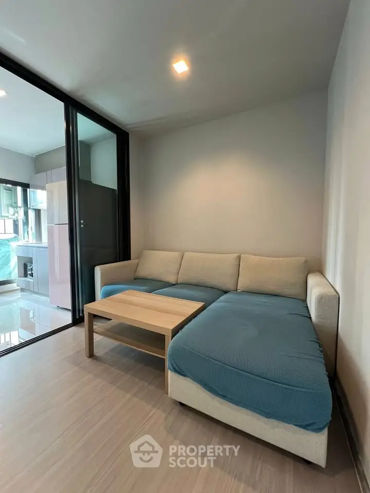 Modern living room with cozy sectional sofa and wooden coffee table, adjacent to a sleek kitchen area.