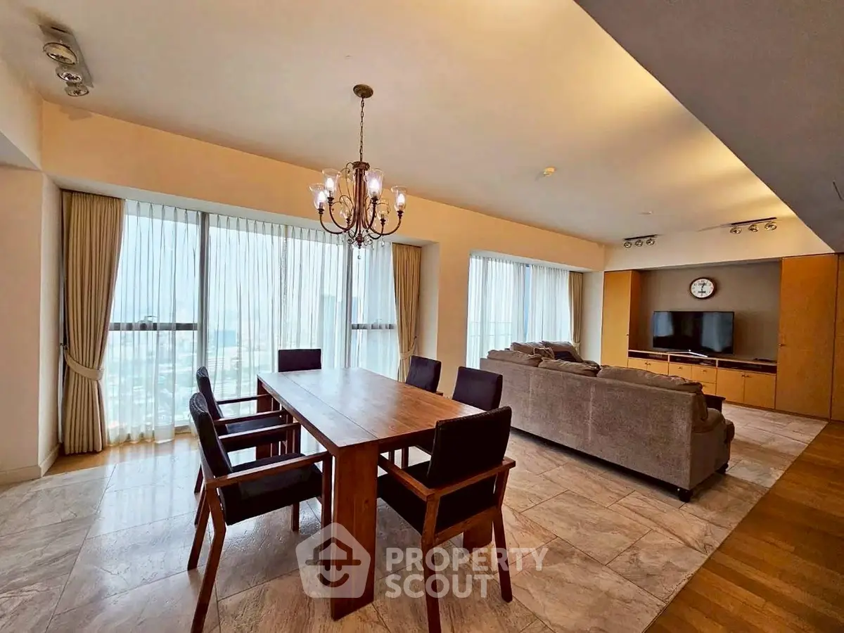 Spacious open-plan living and dining area with elegant chandelier and large windows.
