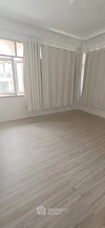 Spacious empty room with large windows and light wood flooring, perfect for customization.