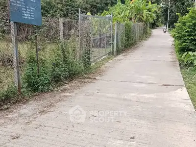 Charming rural pathway with lush greenery and fenced garden, perfect for serene living.