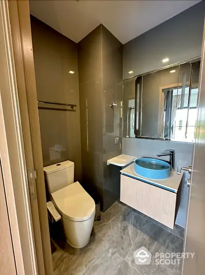 Modern bathroom with sleek design, featuring a unique blue basin, large mirror, and glass shower enclosure, perfect for contemporary living.