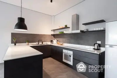 Modern kitchen with sleek black cabinetry and white countertops, featuring an oven and stylish lighting.