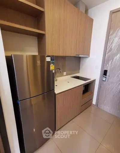 Modern compact kitchen with sleek cabinetry and stainless steel fridge in a stylish apartment.