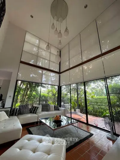 Spacious modern living room with high ceilings and large windows overlooking lush garden.