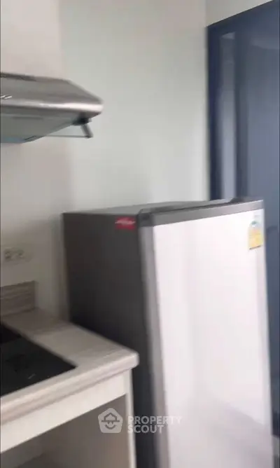 Modern kitchen with sleek appliances and minimalist design, featuring a compact fridge and stovetop.