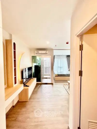 Modern apartment interior with open living room and bedroom, featuring sleek wooden flooring and large windows.