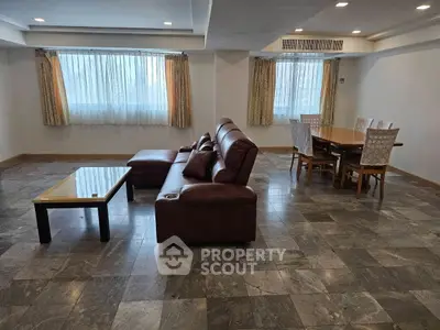 Spacious living room with leather sofa and dining area, featuring large windows and elegant tile flooring.